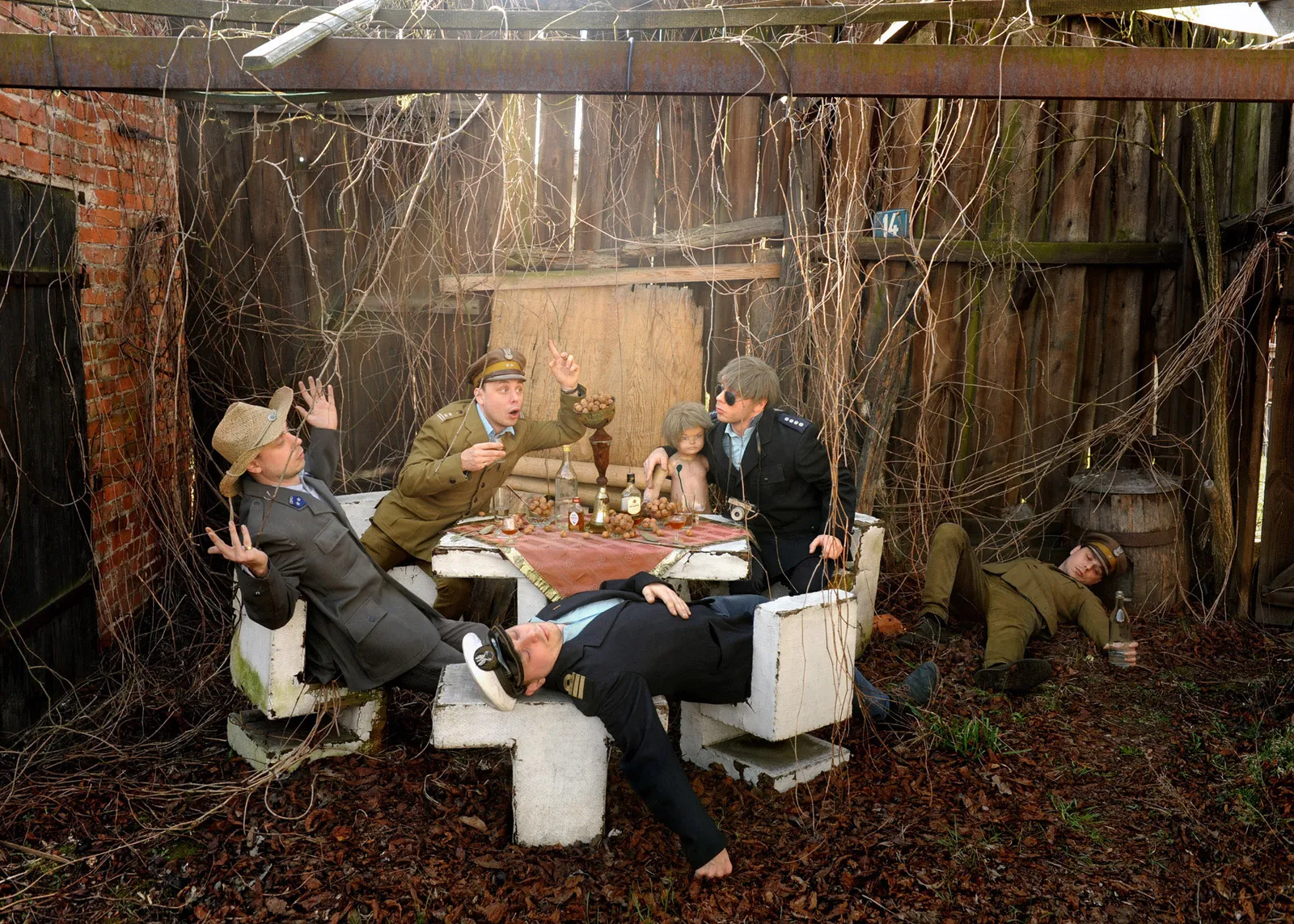 A group of men in uniforms in a chaotic banquet scene at a table amid dry vines